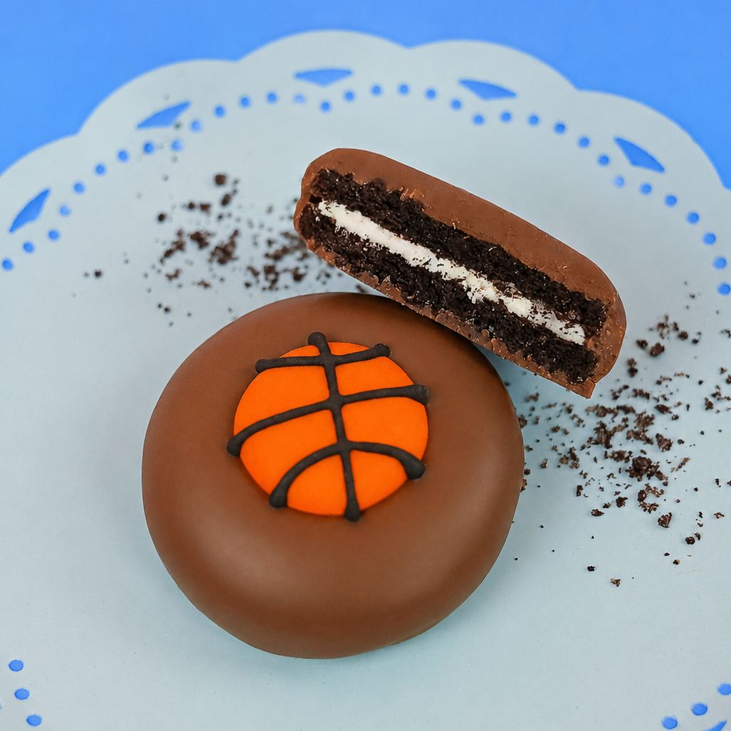 Milk chocolate basketball Oreo showing dark chocolate cookie layers and white cream filling on a mint green plate, handcrafted sports themed chocolate gift by Nibbles and Bits Scranton PA.