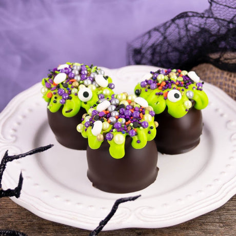 Dark chocolate ganache truffle shaped like a cauldron, dipped in rich dark chocolate and topped with spooky Halloween confetti and candy eyeballs – handmade treat from Nibbles & Bits in Scranton, PA.