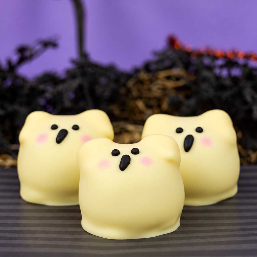 Three white chocolate Ghost Ganache Truffles in a row, each with a hand-painted surprised face and blushed cheeks.