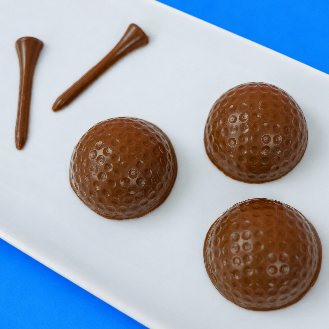 Three solid milk chocolate golf balls with realistic dimple texture and three milk chocolate golf tees on a white rectangular plate with blue background, handmade golf gift set by Nibbles and Bits Scranton PA.