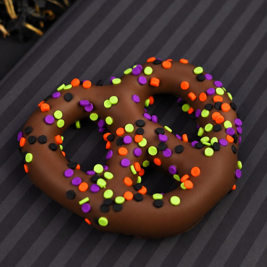 Milk chocolate covered pretzel covered in purple, orange, green and black Halloween sprinkles on a striped background.