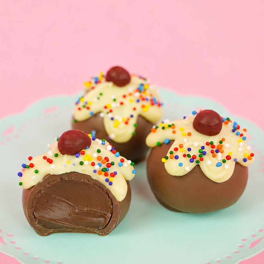 A milk chocolate ganache sundae truffle revealing a rich creamy milk chocolate ganache center alongside two whole decorated truffles on a mint green cake stand, handcrafted celebration gift by Nibbles and Bits Scranton PA.