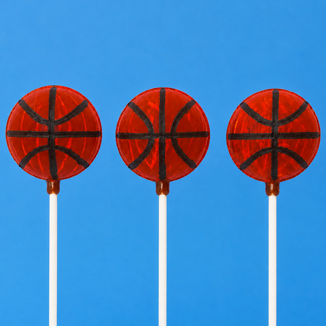 Three milk chocolate ganache truffle pops hand-painted to look like basketballs with orange red coating and black seam lines on white sticks against a blue background, handmade sports gift by Nibbles and Bits Scranton PA.