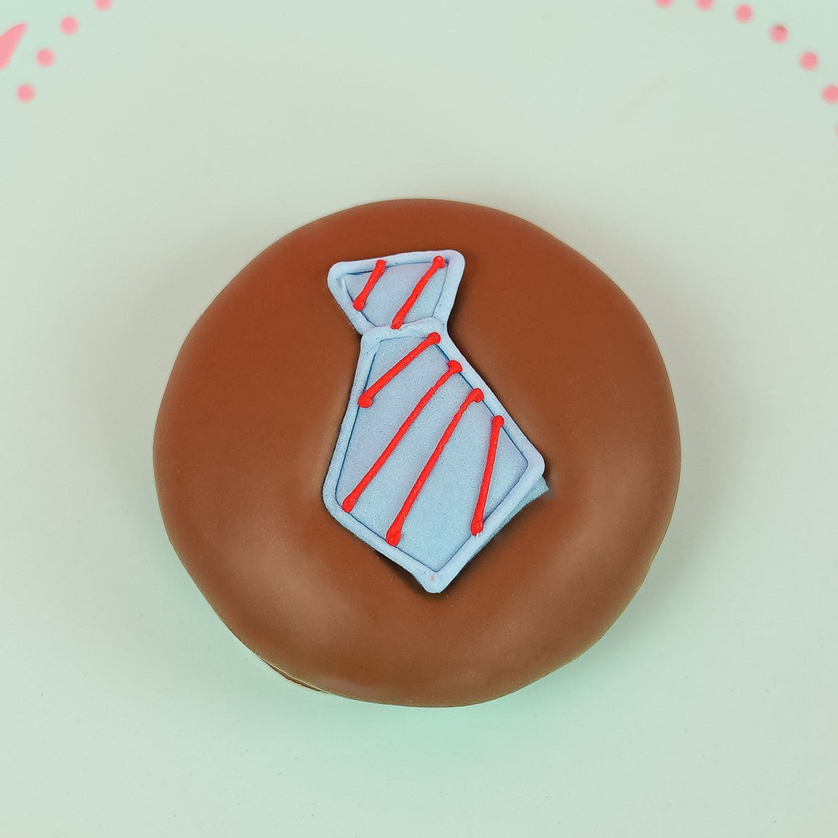 Single milk chocolate covered Oreo decorated with a light blue fondant necktie with hand-piped red diagonal stripes on a mint green decorative plate with pink background, handmade Father's Day gift by Nibbles and Bits Scranton PA.