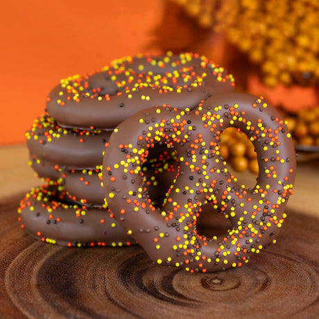 Crunchy Snyder's Olde Tyme pretzels dipped in creamy milk chocolate and topped with festive autumn nonpareil sprinkles – handcrafted fall chocolate treat from Nibbles & Bits.