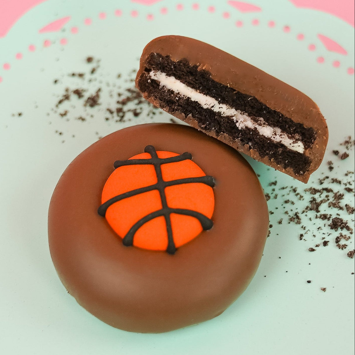 Milk chocolate basketball Oreo showing dark chocolate cookie layers and white cream filling on a mint green plate, handcrafted sports themed chocolate gift by Nibbles and Bits Scranton PA.