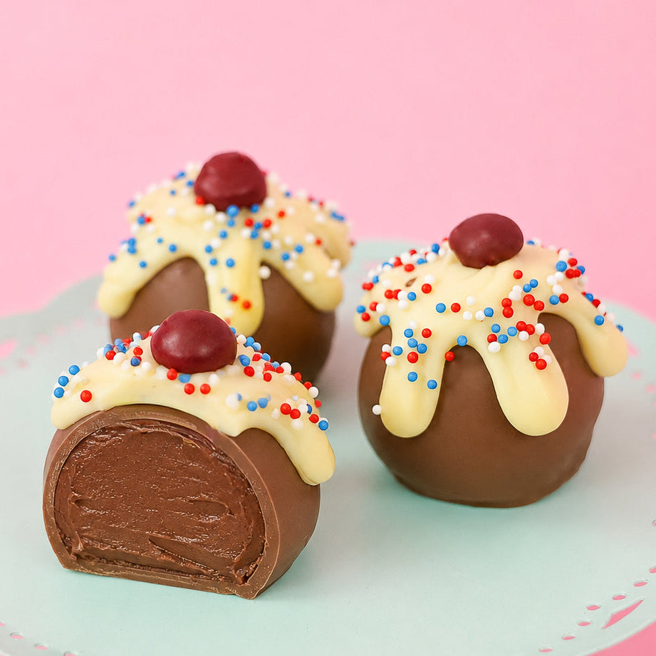 A patriotic sundae milk chocolate ganache truffle revealing a rich creamy milk chocolate ganache center alongside two whole decorated truffles on a mint green cake stand, handcrafted patriotic gift by Nibbles and Bits Scranton PA.