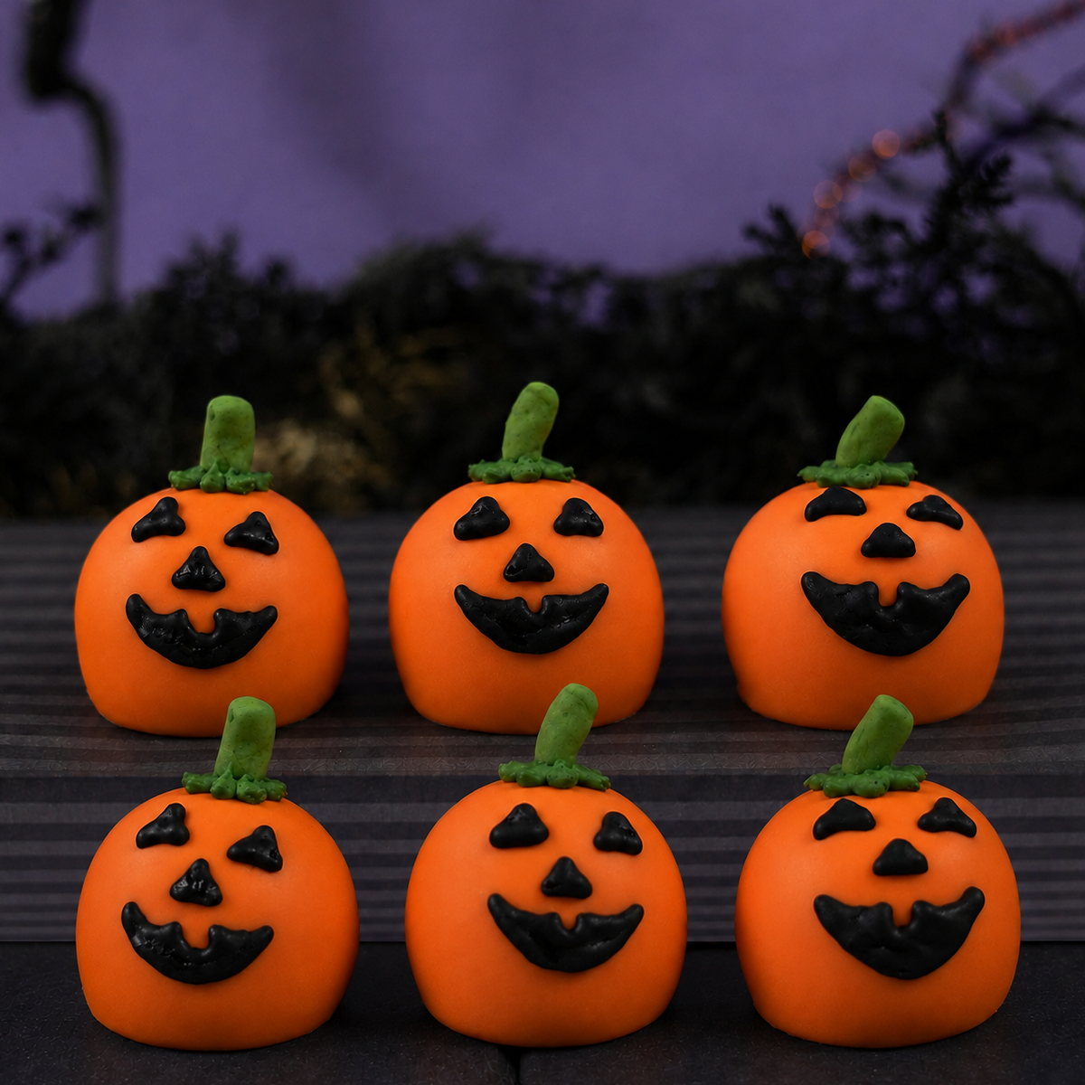 Six Jack O'Lantern Ganache Truffles arranged in two rows, each hand-decorated with a triangle-eyed pumpkin face and green stem.