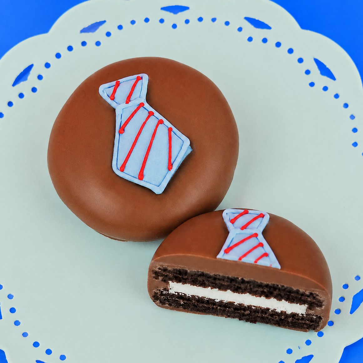 Milk chocolate tie Oreo showing dark chocolate cookie layers and white cream filling alongside whole decorated cookie on a mint green plate, handcrafted Father's Day chocolate gift by Nibbles and Bits Scranton PA.