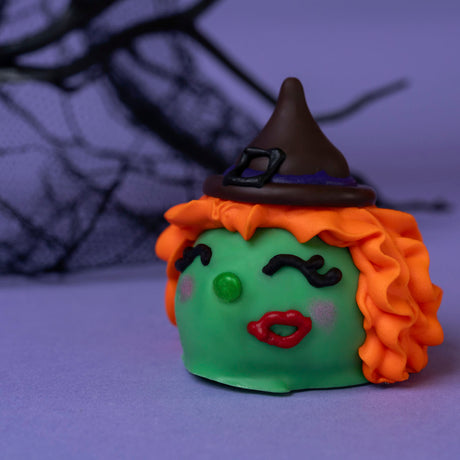 Milk chocolate ganache truffle dipped in white chocolate with a dark chocolate witch’s hat, hand-drawn lashes, button nose, and shimmery blush – handmade Halloween treat from Nibbles & Bits in Scranton, PA.