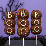 Three Boo! Marshmallow Pops standing upright, each iced with "BOO" and coated in orange, green, purple, and black sprinkles.
