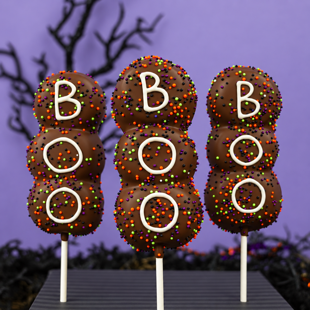 Three Boo! Marshmallow Pops standing upright, each iced with "BOO" and coated in orange, green, purple, and black sprinkles.