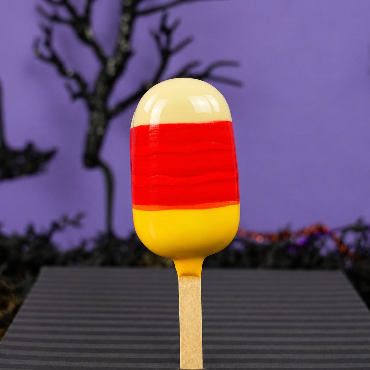 Cake batter ganache pop hand painted like a candy corn on a purple background. 