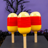 Three candy corn cake batter ganache pops, and painted in yellow orange and red, on a purple halloween background. 