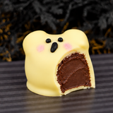 A single Ghost Ganache Truffle with a bite taken out, revealing rich chocolate ganache inside the white chocolate shell.