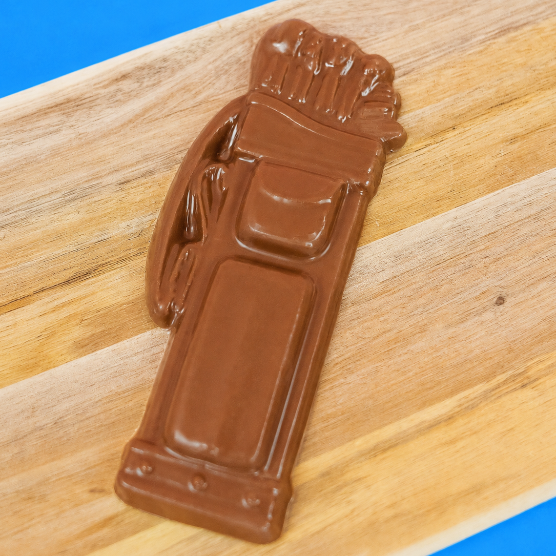 Solid milk chocolate golf bag with detailed molded clubs, pockets and straps displayed on a rustic wood board with blue background, handmade gift for golfers by Nibbles and Bits Scranton PA.