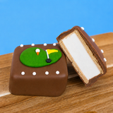A milk chocolate golf green s'more revealing thick homemade vanilla marshmallow layer and golden graham cracker base alongside a whole decorated s'more on a wood board with blue background, handcrafted golf gift by Nibbles and Bits Scranton PA.