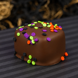 Homemade vanilla marshmallow covered in milk chocolate topped with Halloween confetti sprinkles in orange, green, purple and black, on a striped plate with a purple backdrop. 