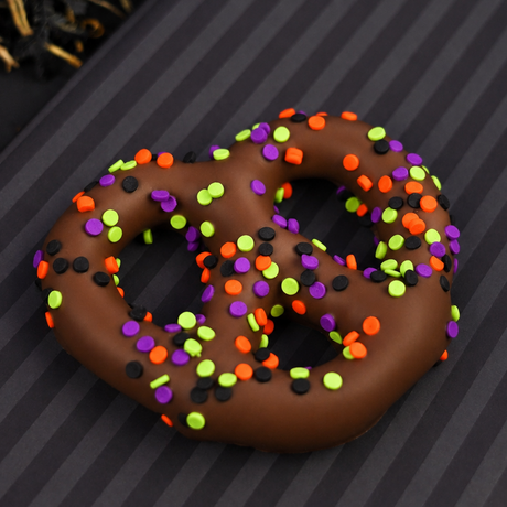Milk chocolate covered pretzel covered in purple, orange, green and black Halloween sprinkles on a striped background. 