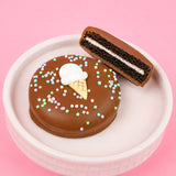 Milk chocolate ice cream cone Oreo showing dark chocolate cookie layers and white cream filling alongside whole decorated cookie in a pink bowl with pink background, handcrafted summer treat by Nibbles and Bits Scranton PA.