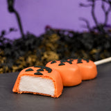 Three homemade vanilla marshmallows on a stick dipped in orange chocolate and hand decorated with jack o lantern faces, cut open to show marshmallow filling. 