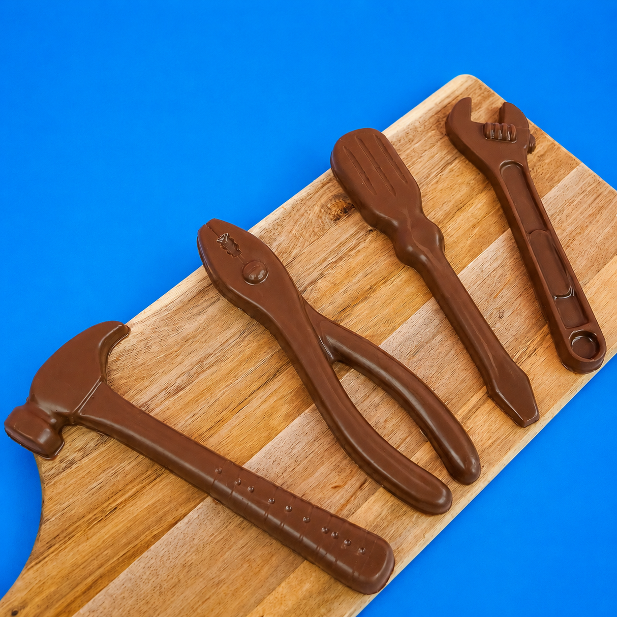 Four large solid milk chocolate tools including a hammer pliers screwdriver and wrench displayed on a rustic wood board with blue background, handmade Father's Day gift set by Nibbles and Bits Scranton PA.