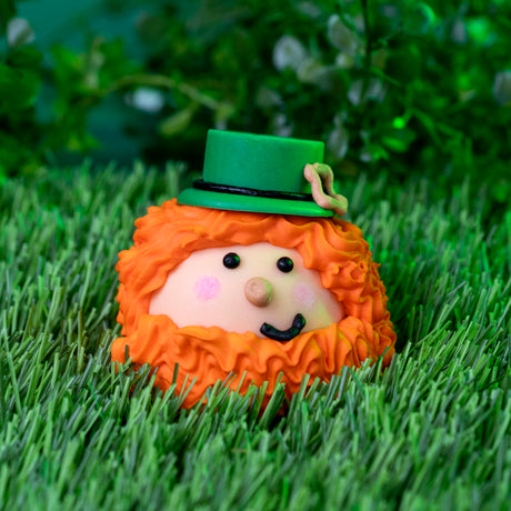 White chocolate–covered milk chocolate ganache truffle shaped like a whimsical leprechaun with a crooked smile for St. Patrick’s Day.