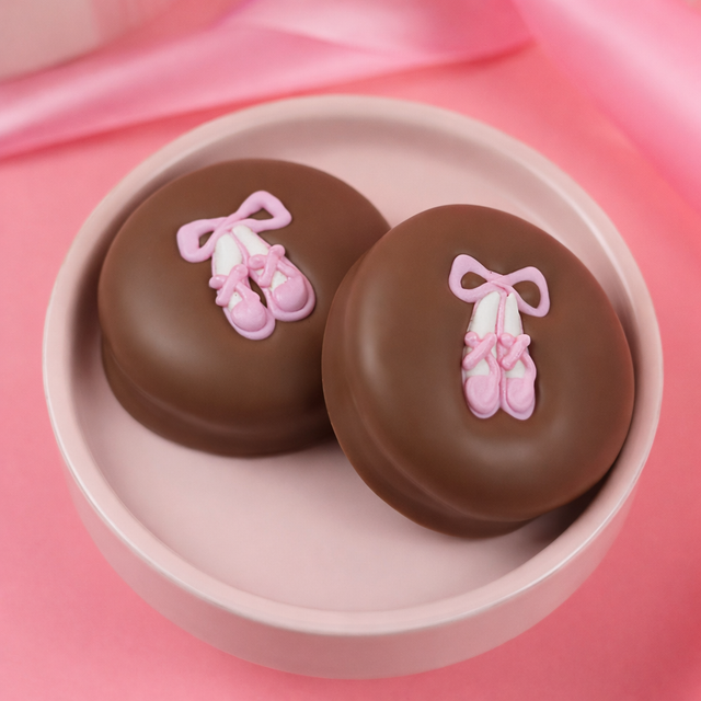 Milk chocolate covered sandwich cookies topped with pink ballet slipper decorations displayed in a soft pink dish.