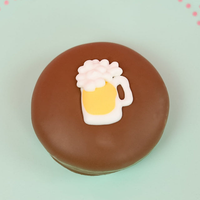 Single milk chocolate covered Oreo decorated with a fondant beer mug overflowing with white frothy foam on a mint green decorative plate with pink background, handmade adult novelty gift by Nibbles and Bits Scranton PA.