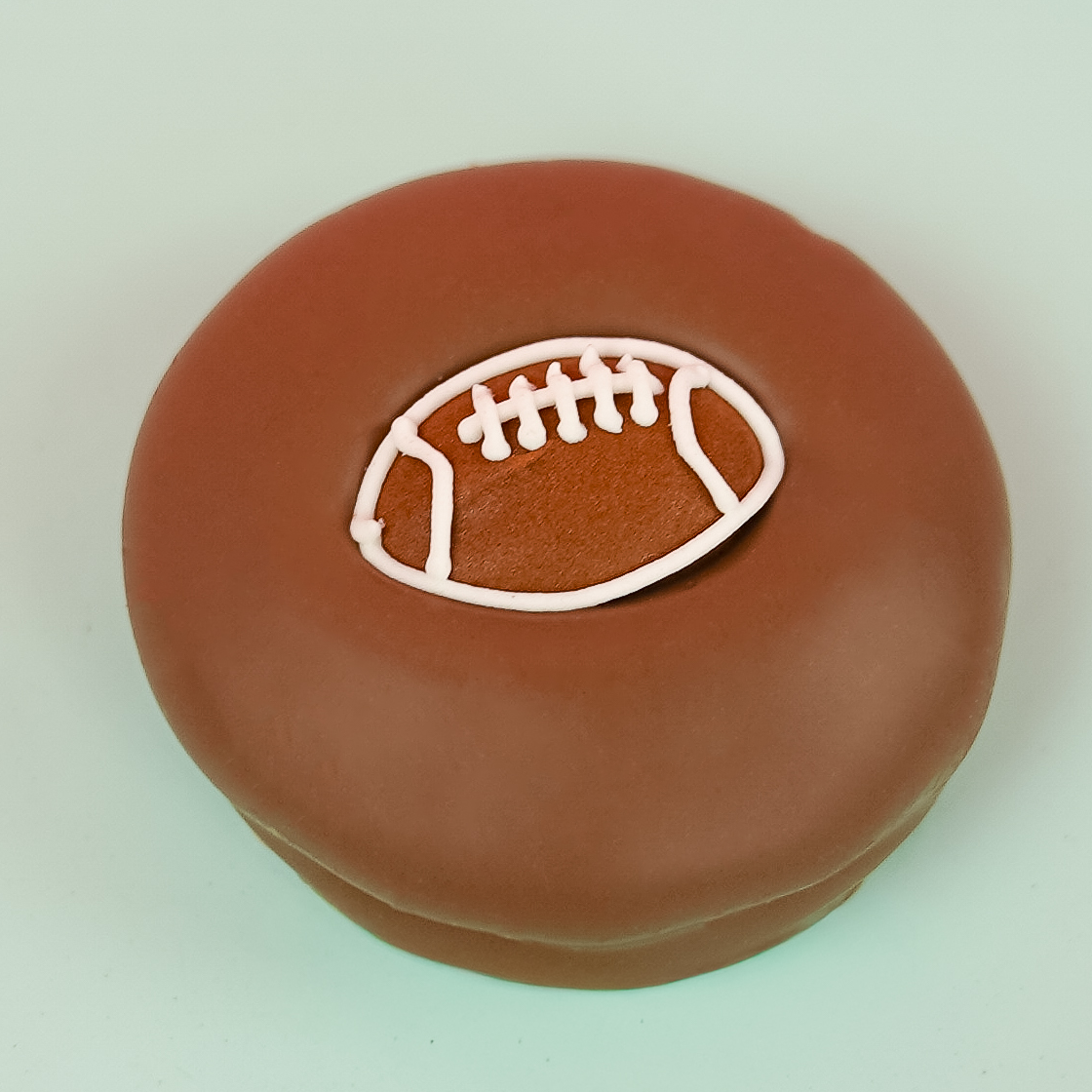 Milk chocolate football Oreo with dark chocolate cookie layers and white cream filling on a mint green plate, handcrafted sports themed chocolate gift by Nibbles and Bits Scranton PA.