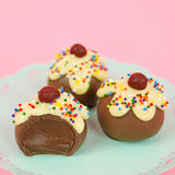 A milk chocolate ganache sundae truffle revealing a rich creamy milk chocolate ganache center alongside two whole decorated truffles on a mint green cake stand, handcrafted celebration gift by Nibbles and Bits Scranton PA.