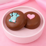 Two milk chocolate covered Oreos in a pink bowl, one decorated with teal fondant scrubs and stethoscope, one with a pink heart, with a cross-section showing cookie and cream filling, nurse appreciation gift by Nibbles & Bits. 