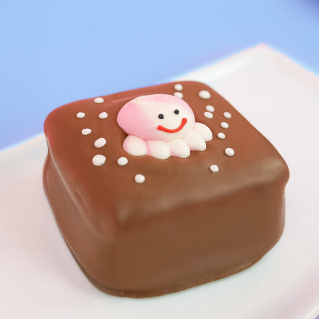 Single milk chocolate octopus s'more on a white plate with blue background, topped with an adorable pink fondant octopus with red smile expressive eyes and white tentacles surrounded by white bubble dot decorations, handmade ocean themed treat by Nibbles and Bits Scranton PA.