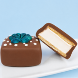 A milk chocolate seashell s'more revealing thick homemade vanilla marshmallow layer and golden graham cracker base alongside a whole s'more decorated with a metallic teal fondant scallop shell on a white plate with blue background, handcrafted ocean treat by Nibbles and Bits Scranton PA.