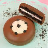 Milk chocolate soccer ball Oreo showing dark chocolate cookie layers and white cream filling on a mint green plate with pink background, handcrafted sports themed chocolate gift by Nibbles and Bits Scranton PA.
