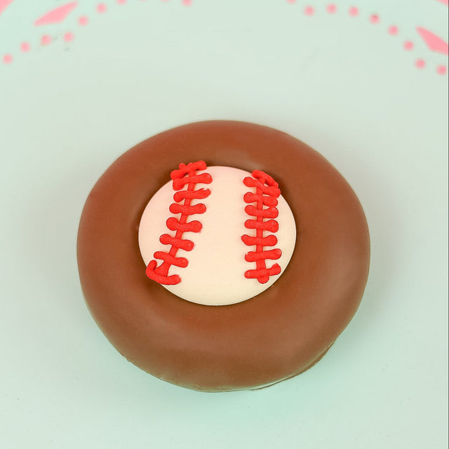 Single milk chocolate covered Oreo decorated with a white fondant baseball and hand-piped red lace stitching on a mint green decorative plate with pink background, handmade sports gift by Nibbles and Bits Scranton PA.