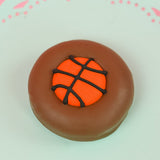 Single milk chocolate covered Oreo decorated with a vibrant orange fondant basketball with dark chocolate seam lines on a mint green decorative plate with pink background, handmade sports gift by Nibbles and Bits Scranton PA.