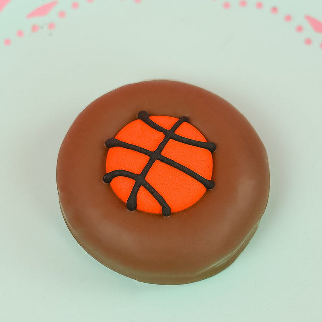 Single milk chocolate covered Oreo decorated with a vibrant orange fondant basketball with dark chocolate seam lines on a mint green decorative plate with pink background, handmade sports gift by Nibbles and Bits Scranton PA.