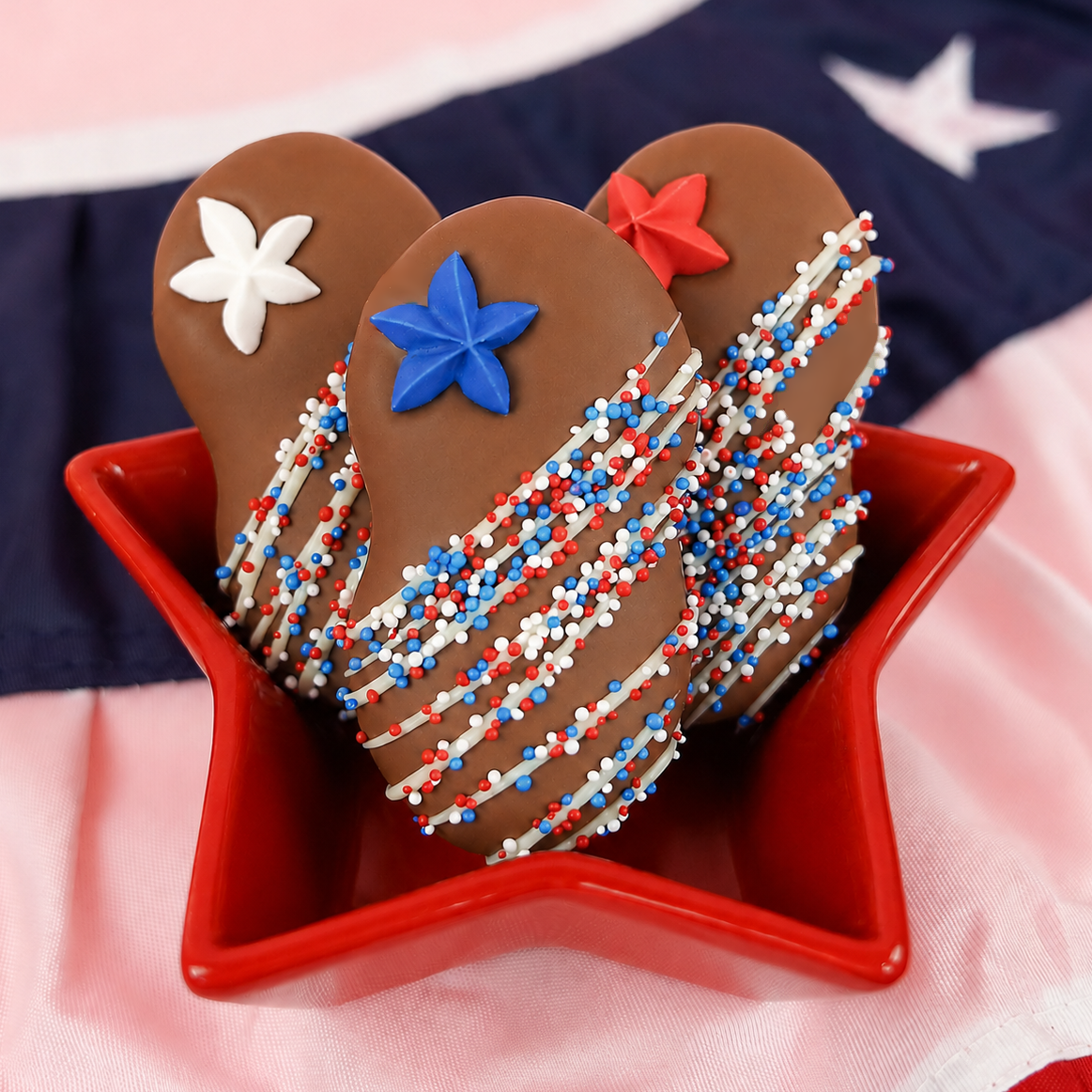 Close-up of milk chocolate Nutter Butter cookie topped with a blue fondant star decal and red, white and blue nonpareils with white chocolate drizzle, patriotic Fourth of July treat by Nibbles and Bits.