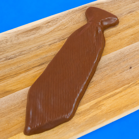 Solid milk chocolate necktie with diagonal stripe texture and molded knot displayed on a rustic wood board with blue background, handmade Father's Day gift by Nibbles and Bits Scranton PA.