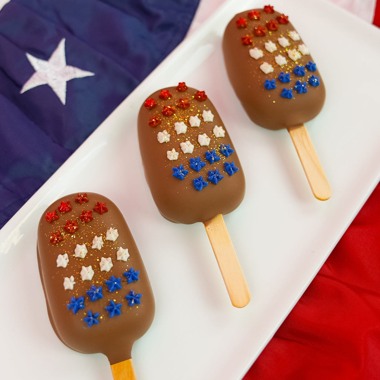 A patriotic milk chocolate peanut butter pop revealing a thick creamy handmade peanut butter ganache center encased in smooth milk chocolate with star confetti decoration, gourmet summer treat by Nibbles and Bits Scranton PA.