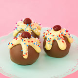Three patriotic sundae milk chocolate ganache truffles on a mint green cake stand with pink background, each topped with dripping white chocolate, red, white and blue nonpareils and a dark chocolate cherry, handmade Fourth of July gift by Nibbles and Bits Scranton PA.
