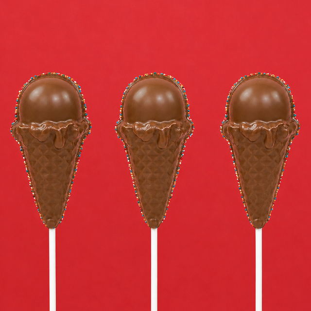 Three solid milk chocolate ice cream cone pops showing detailed molded waffle cone and rounded scoop with patriotic nonpareil border on white sticks against a red background, handmade summer treat by Nibbles and Bits Scranton PA.