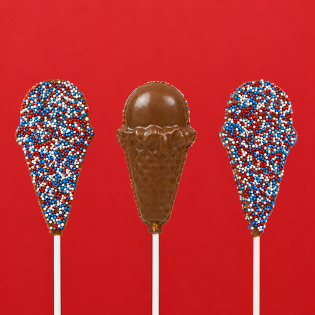 Three solid milk chocolate patriotic ice cream cone pops on white sticks against a bold red background showing both the red, white and blue nonpareil covered side and the detailed molded waffle cone and scoop side, handmade Fourth of July treat by Nibbles and Bits Scranton PA.