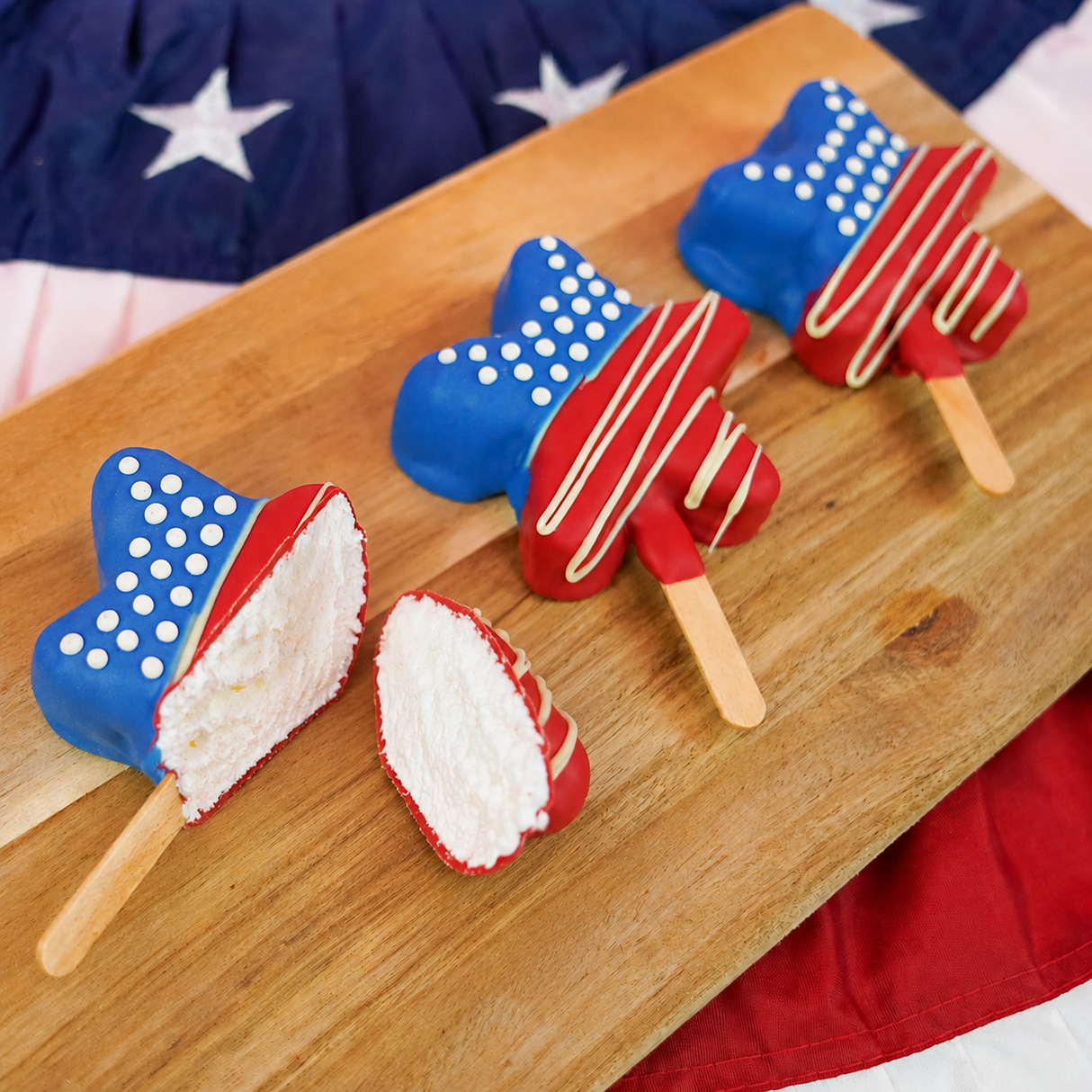 Handmade vanilla marshmallow star pop dipped in white chocolate and decorated with blue field white dots and red stripes drizzled in white chocolate, patriotic Fourth of July treat by Nibbles & Bits.