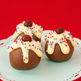 Three patriotic sundae milk chocolate ganache truffles on a mint green cake stand with red background, each topped with dripping white chocolate, red, white and blue nonpareils and a dark chocolate cherry, handmade Fourth of July gift by Nibbles and Bits Scranton PA.