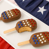 A patriotic milk chocolate peanut butter pop revealing a thick creamy handmade peanut butter ganache center encased in smooth milk chocolate with star decoration, gourmet summer treat by Nibbles and Bits Scranton PA.