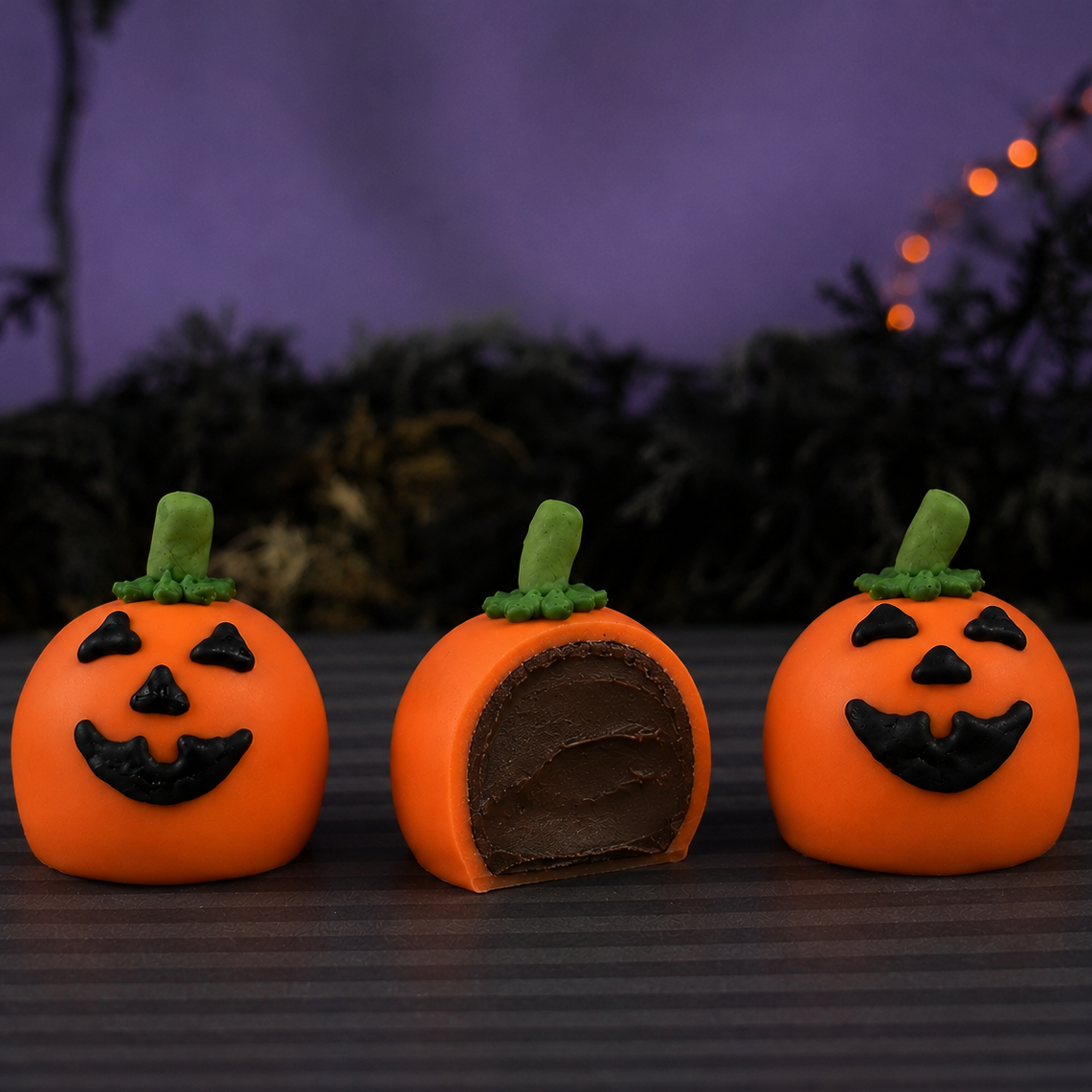 Three Jack O'Lantern Ganache Truffles, one cut in half revealing rich chocolate ganache filling inside the orange chocolate shell.