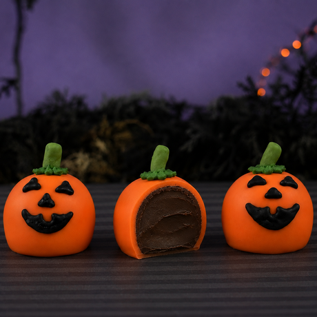 Three Jack O'Lantern Ganache Truffles, one cut in half revealing rich chocolate ganache filling inside the orange chocolate shell.