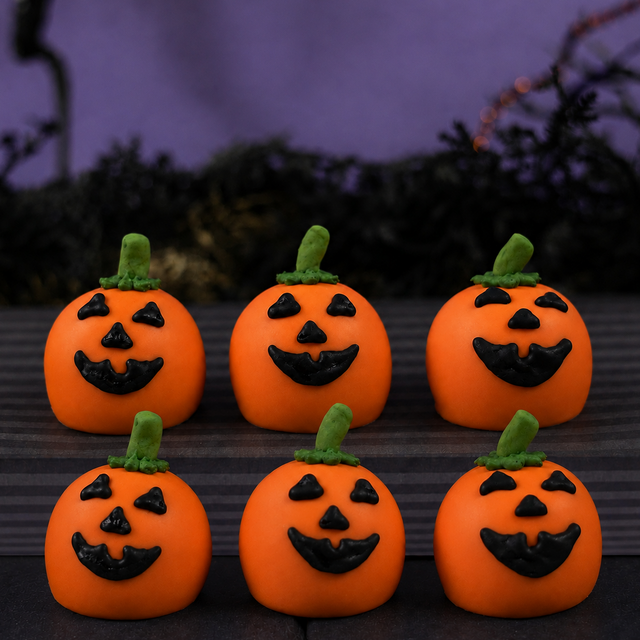 Six Jack O'Lantern Ganache Truffles arranged in two rows, each hand-decorated with a triangle-eyed pumpkin face and green stem.